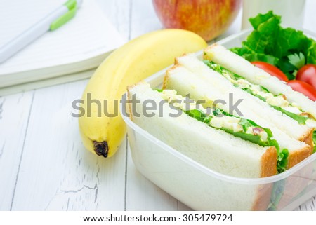 Lunch box with egg salad sandwiches, fruits, milk and stationery