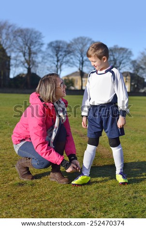 Mother helping her young boy tie his football boot laces.