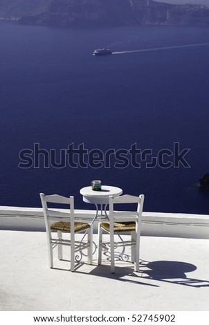 Table and chairs overlooking on a clear day at Santorini, Greece with ship in the background.