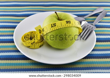 Green apple and yellow measuring tape concept for healthy diet and body weight control.