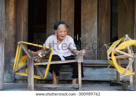 NAMDINH, VIETNAM - Jun 14, 2015: An elderly woman sitting roll of yellow silk with crude homemade instruments. This is the place preserved in a manner weaving tradition exists very little in VIETNAM