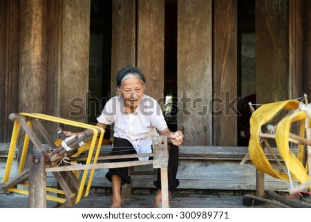 NAMDINH, VIETNAM - Jun 14, 2015: An elderly woman sitting roll of yellow silk with crude homemade instruments. This is the place preserved in a manner weaving tradition exists very little in VIETNAM