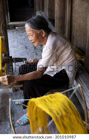 Namdinh, Vietnam - Jun 14, 2015: An elderly woman sitting roll of yellow silk with crude homemade instruments. This is the place preserved in a manner weaving tradition exists very little in Vietnam