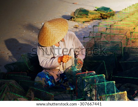 NAMDINH, VIETNAM - Aug 15, 2015: The man is mending his nets on the shore in Namdinh, Vietnam.