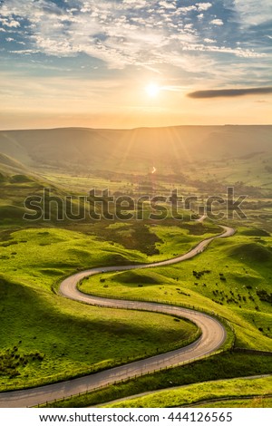 A long and winding road passing through green hills at sunset.
