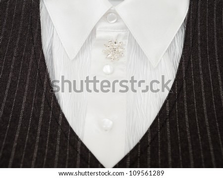 a ladies suit - a white blouse with a glass brooch and a black jacket, closeup