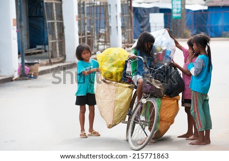 SIEM REAP, CAMBODIA - JUNE 28, 2014: Four local unidentified girls of school age arrange large bags with different kinds of trash on a bicycle. In Khmer family every member must earn money.