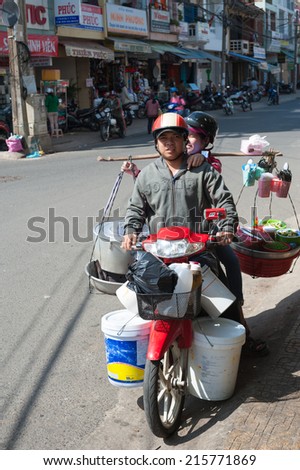 DALAT, VIETNAM - JUNE 8: Unidentified woman and man on a motorbike stand at a roadside. The woman holds a yoke with cooked food and kitchen utensils.