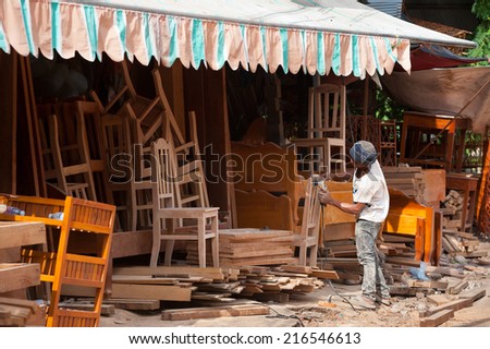 SIEM REAP, CAMBODIA - JUNE 28, 2014: An unidentified local cabinet maker grinds a chair of mahogany with a grinding machine.