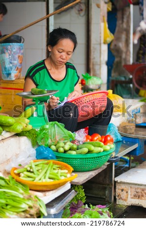 HO CHI MINH, VIETNAM - JULY 5, 2014:  An unidentified vegetable seller at Ben Thanh market writes something in her notebook. While tourists search here souvenirs townspeople come to buy fresh food.