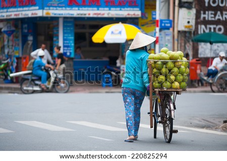 HO CHI MINH, VIETNAM - JULY 6, 2014: An unidentified street hawker rolls her bicycle with a basket full of pomelo fruit, the Pham Ngu Lao area.