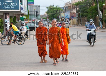 SIEM REAP, CAMBODIA - JUNE 28, 2014: Three unidentified young Buddhist monks walk in the downtown. Theravada Buddhism is the official religion of Cambodia, practiced by 95 percent of the population.