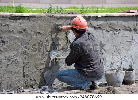 a worker applies plaster to a wall, outdoors