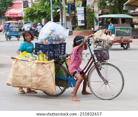 SIEM REAP, CAMBODIA - JUNE 28, 2014: Two local unidentified girls of school age pose for camera carrying large bags with trash on a bicycle. In Khmer family every member must earn money.