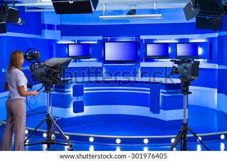 woman cameraman works at empty blue TV studio
