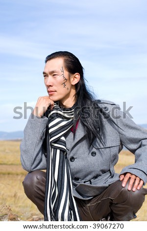 Young asian man in grey coat and striped black-and-white scarf. The tracery on his cheek is his name Chinghis in ancient Mongolian.