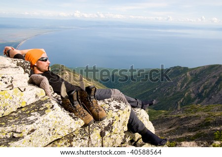 young man rests on stone having climbed up mountain top