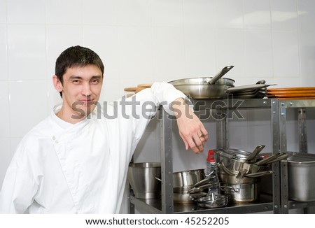 european chef leans on utensils rack looking into camera in restaurant kitchen