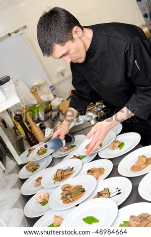 male caucasian chef in black uniform pours sauce on plates with lamb meat
