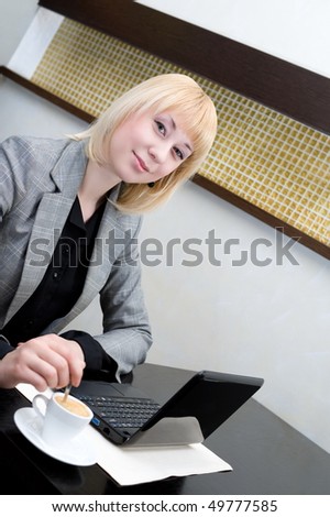 young businesswoman stirs coffee in cup at table with netbook