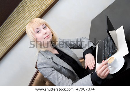 young businesswoman stirs coffee in cup at table with netbook