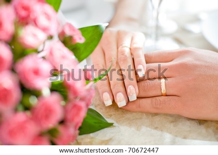 hands of a bride and a bridegroom, just married, a bridal bouquet is beside