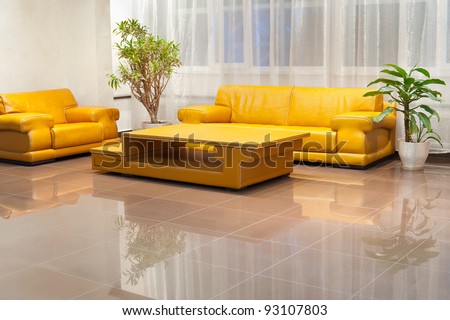 a yellow wide leather sofa, an armchair and a coffee table in hall interior
