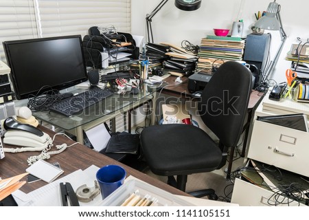 Messy business office desk with piles of files and disorganized clutter.