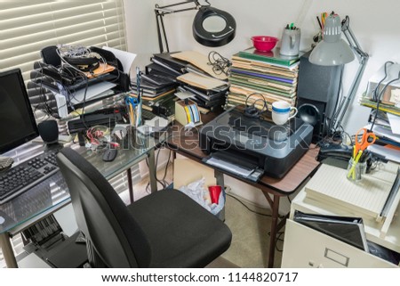 Messy office desk and table with piles of files and disorganized clutter.
