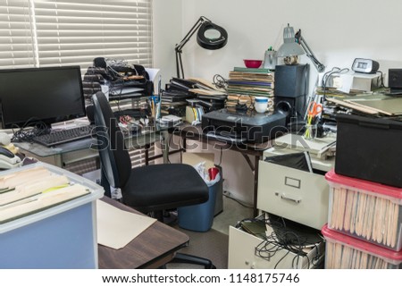 Messy business office desk with boxes of files and disorganized clutter.