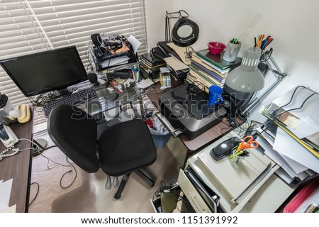 Messy office desk with stacks of files and disorganized clutter.