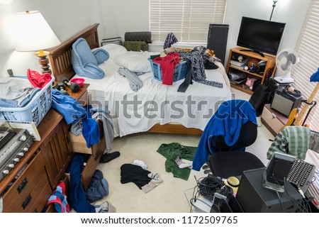 Very messy, cluttered teenage boy\'s bedroom with piles of clothes, music and sports equipment.