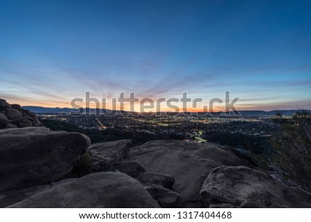 Rocky hilltop predawn view of San Fernando Valley neighborhoods and the San Gabriel Mountains in the city of Los Angeles, California.