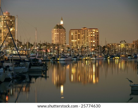 Apartment buildings and boats reflect in a quiet marina at night.