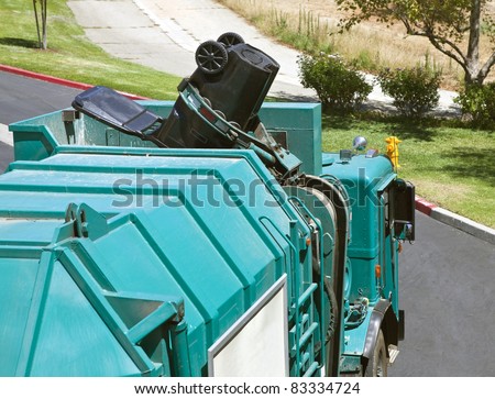 Municipal robotic arm trash truck dumps a large black can.