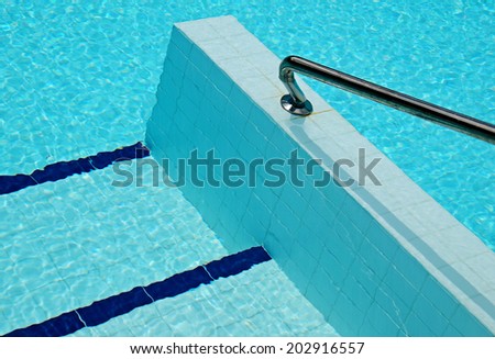 Hand rail at entrance to a swimming pool with ripples on water surface producing an abstract background.