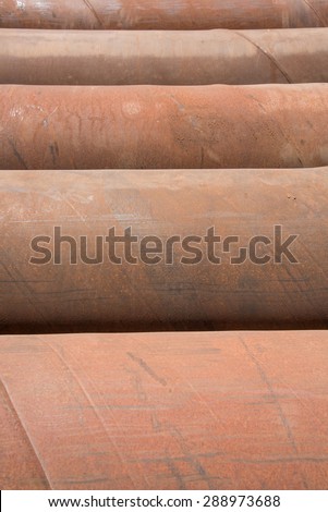 Five large iron pipes, rusted and laying side by side