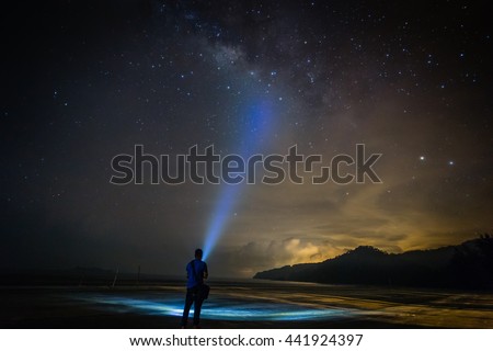 Landscape with Milky Way. Night sky with stars and silhouette of a standing happy man on the beach with the torchlight