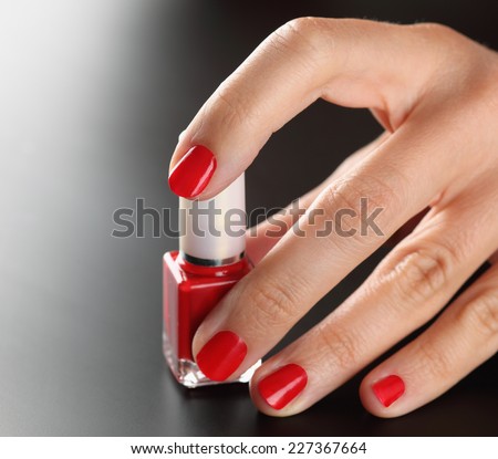 Red bottle of nail polish in manicured woman palms on black background.