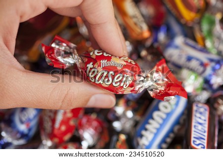 Paphos, Cyprus - December 19, 2013 Woman\'s hand holding Maltesers Teasers candy against background of candies manufactured by Mars, Incorporated.
