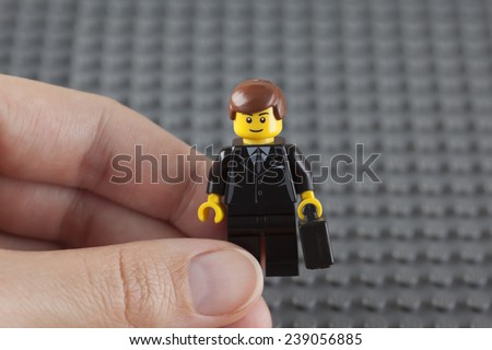 Tambov, Russian Federation - July 26, 2014 Lego businessman minifigure in blue suit with black suitcase in human hand on Lego grey baseplate background. Studio shot.