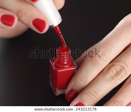 Open red bottle of nail polish in manicured woman palms on black background.