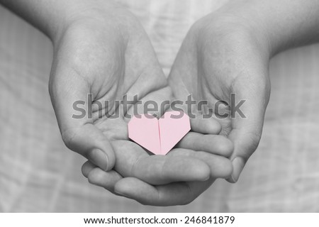 Pink origami heart in human hands. Black and white.