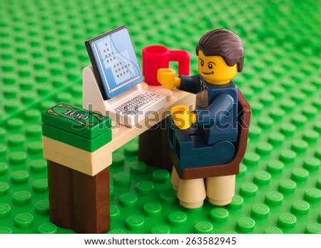 Tambov, Russian Federation - March 24, 2015 Lego businessman sits at his working table with computer, money and cup on Lego green baseplate background. Studio shot.