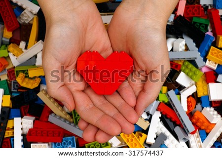 Tambov, Russian Federation - September 07, 2015 Lego red heart in woman hands with Lego blocks background. Studio shot.
