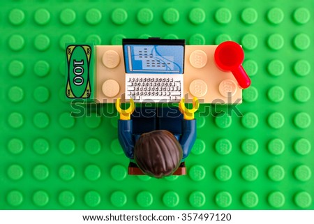 Tambov, Russian Federation - March 24, 2015 Lego businessman sits at his working table with computer, money and cup on Lego green baseplate background. Top view. Studio shot.