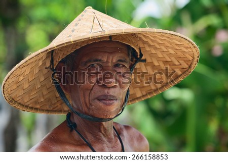 BALI, INDONESIA - MARCH 20: Portrait of unidentified old Balinese farmer with a wrinkled face in traditional straw wide-brimmed hat during harvesting crop in rice terraces in Bali on 20 March, 2015