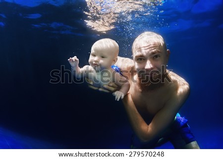 In blue pool father swim underwater with 5 month old baby son - dive deep into clear water with cheerful boy, healthy family lifestyle, child swimming activity and physical growth and development