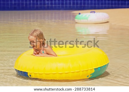 Funny portrait of cheerful baby girl swimming with fun on yellow tube in aqua park pool. Healthy active family lifestyle, and children water sports activity with parents on summer vacation with kids