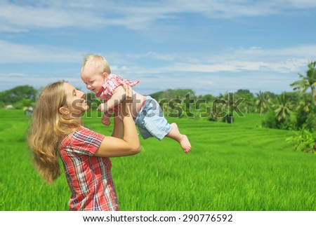 Happy mother tossing up joyful baby boy on Balinese green rice terraces background. Outdoors healthy child activity, active lifestyle on family summer vacation with son on Indonesian tropical island